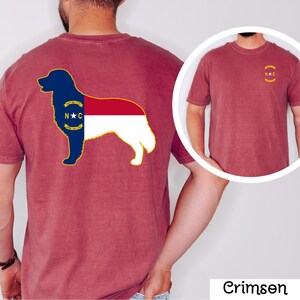 Puede incluir: Camiseta de color carmes&iacute; con la silueta de un perro con el dise&ntilde;o de la bandera del estado de Carolina del Norte en la espalda. El dise&ntilde;o de la bandera es azul, rojo, blanco y dorado. Una versi&oacute;n m&aacute;s peque&ntilde;a de la bandera est&aacute; en la parte delantera.