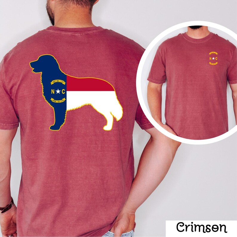 Puede incluir: Camiseta de color carmes&iacute; con la silueta de un perro con el dise&ntilde;o de la bandera del estado de Carolina del Norte en la espalda. El dise&ntilde;o de la bandera es azul, rojo, blanco y dorado. Una versi&oacute;n m&aacute;s peque&ntilde;a de la bandera est&aacute; en la parte delantera.