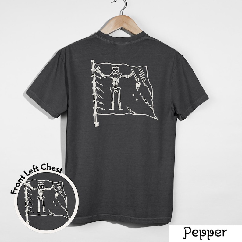 May include: Dark gray t-shirt with a white pirate flag design on the back. The flag features a skeleton figure holding a sword and a heart. A smaller version of the design is on the front left chest. The word "Pepper" is at the bottom.