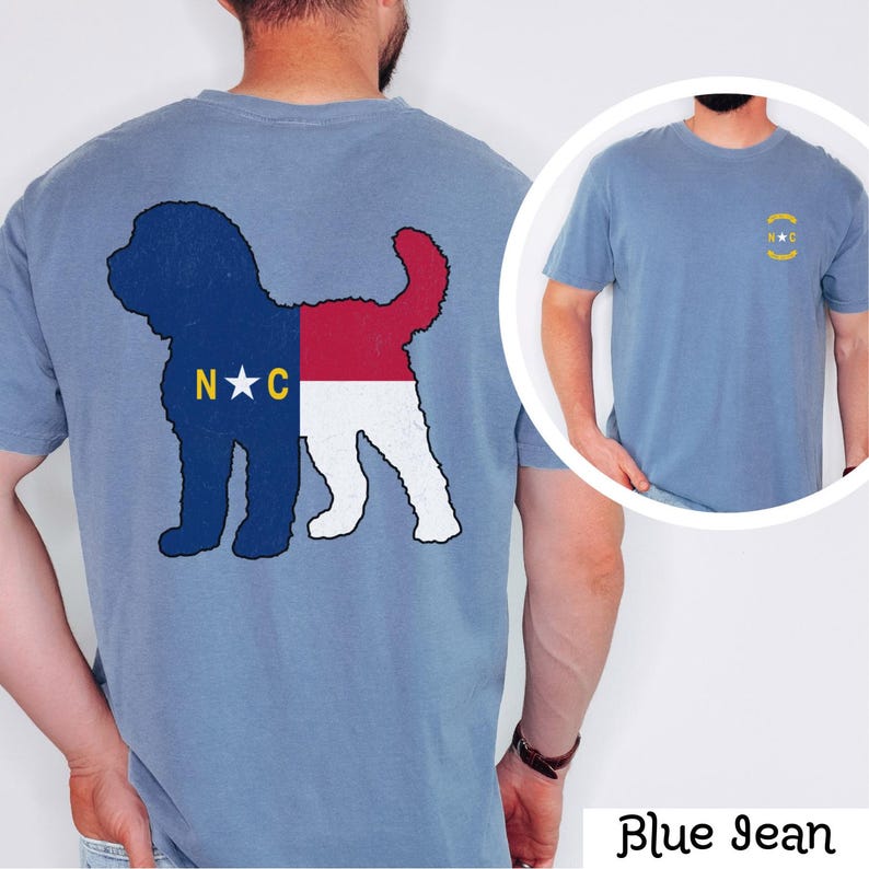 May include: A blue jean t-shirt featuring a silhouette of a dog with the North Carolina state flag colours. The back of the shirt has the silhouette of the dog with the North Carolina state flag colours. The front of the shirt has a small circle with the letters "N.C." in gold.