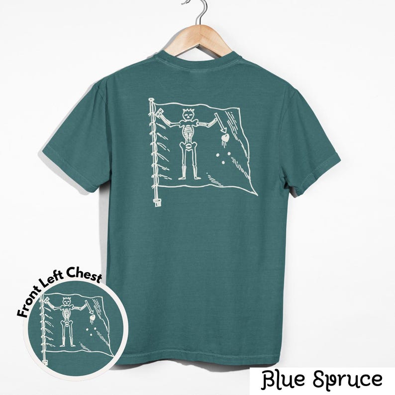May include: Blue spruce t-shirt with a white skeleton pirate flag design on the back. The shirt has a crew neck and short sleeves. A smaller version of the flag design is on the front left chest. The words "Blue Spruce" are at the bottom.