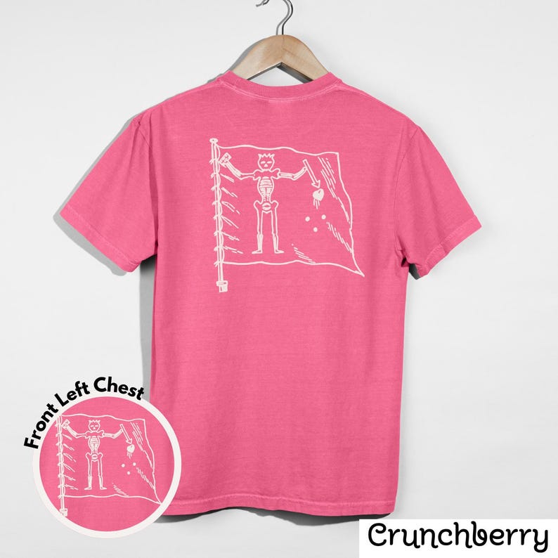 May include: A pink t-shirt with a white graphic of a skeleton holding a sword and a heart on a flag. The shirt has short sleeves and a crew neck. The text "Crunchberry" is at the bottom right.