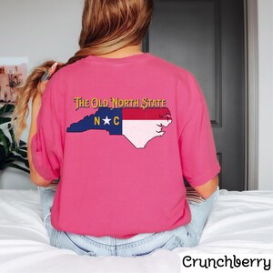 May include: Pink t-shirt with a graphic of the North Carolina state flag and the text "The Old North State" in yellow.