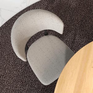 May include: A light gray curved chair with a dark gray fabric seat and back. The chair is sitting on a dark gray carpet.