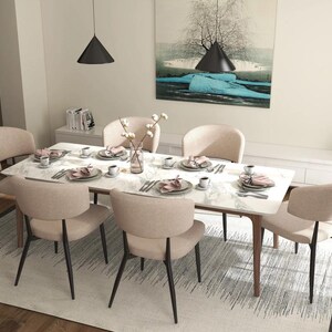 May include: A white marble dining table with six beige chairs. The table is set with place settings, including plates, napkins, and silverware. There is a vase of white flowers in the center of the table.