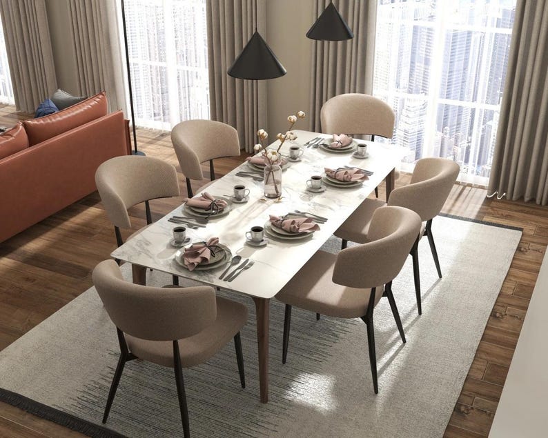 May include: A white marble dining table with six beige chairs. The table has a modern design with a sleek, minimalist look. The chairs are upholstered in a soft, neutral fabric.