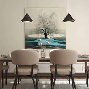 May include: A dining room with a wooden table and six chairs. The chairs are upholstered in a light brown fabric and have black metal legs. Two black pendant lights hang above the table. A large painting of a tree with blue water and white cotton balls hangs on the wall behind the table.