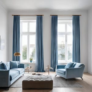 Op de afbeelding: Een woonkamer met twee grote ramen met blauwe gordijnen, een blauwe bank, een blauwe fauteuil en een grijze poef. De kamer heeft een lichte houten vloer en een wit plafond.