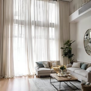 Peut inclure: Un salon lumineux et aéré avec de longs rideaux crème transparents encadrant de grandes fenêtres. Deux canapés de couleur claire, une table basse en bois et un grand miroir complètent l'espace. Un tapis et des plantes ajoutent de la chaleur.