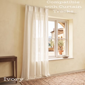 Puede incluir: Una cortina de color marfil con pliegues cuelga de una barra met&aacute;lica sobre una ventana. El texto "Compatible with Curtain Tracks" es visible en la parte superior y la palabra "Ivory" aparece en la parte inferior izquierda.