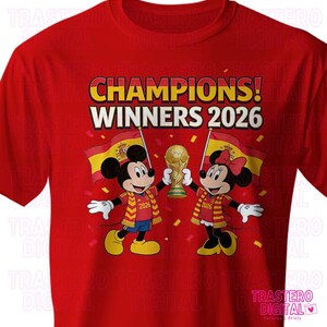 May include: A bright red t-shirt featuring a graphic of Mickey and Minnie Mouse holding a gold trophy. The text reads CHAMPIONS! WINNERS 2026. The characters wear red and yellow scarves and stand in front of two Spanish flags with confetti falling.