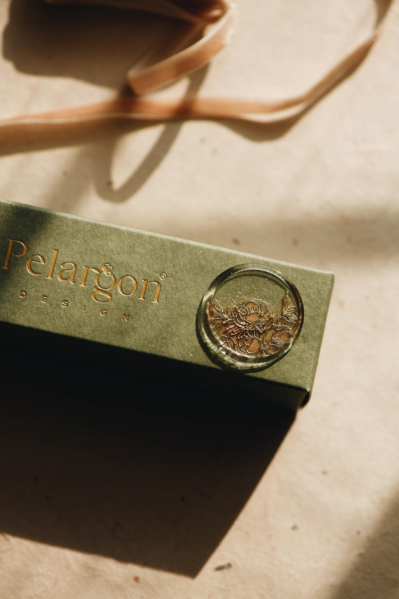 May include: A green box with the text "Pelargon Design" on the top. A clear wax seal with a gold floral design is on the box.
