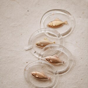 May include: Four clear glass coasters with gold fish designs. Each coaster features a different fish design.