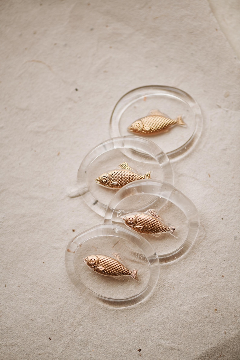 May include: Four clear glass coasters with gold fish designs. Each coaster features a different fish design.