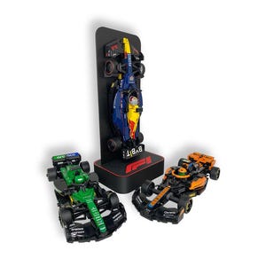 Peut inclure: Trois modèles réduits de voitures de course de Formule 1 en vert, orange et bleu avec des détails noirs. Une voiture est exposée sur un présentoir noir avec le logo F1. Les voitures présentent des logos de sponsors et des designs complexes.