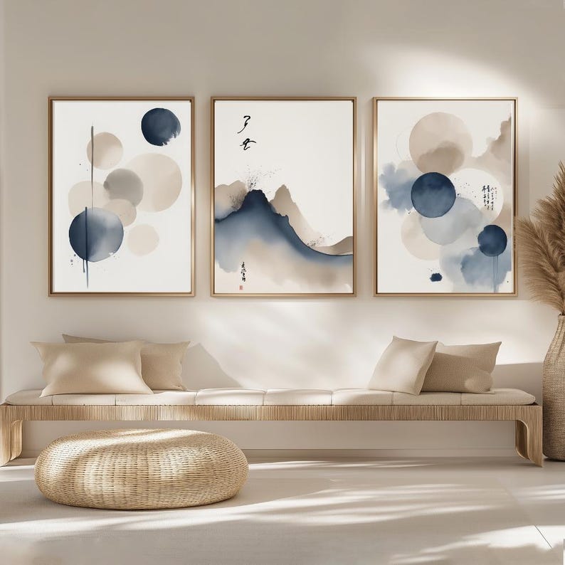 May include: Three framed watercolour art prints. Each print features abstract designs in shades of blue, beige, and grey. The artwork includes circles and mountain-like shapes, with some prints featuring Japanese calligraphy. The frames are a light brown colour.