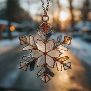 May include: A stained glass snowflake ornament with a gold-colored metal frame and chain. The snowflake features various colors, including clear, blue, and amber glass pieces. The ornament is hanging in front of a blurred background.