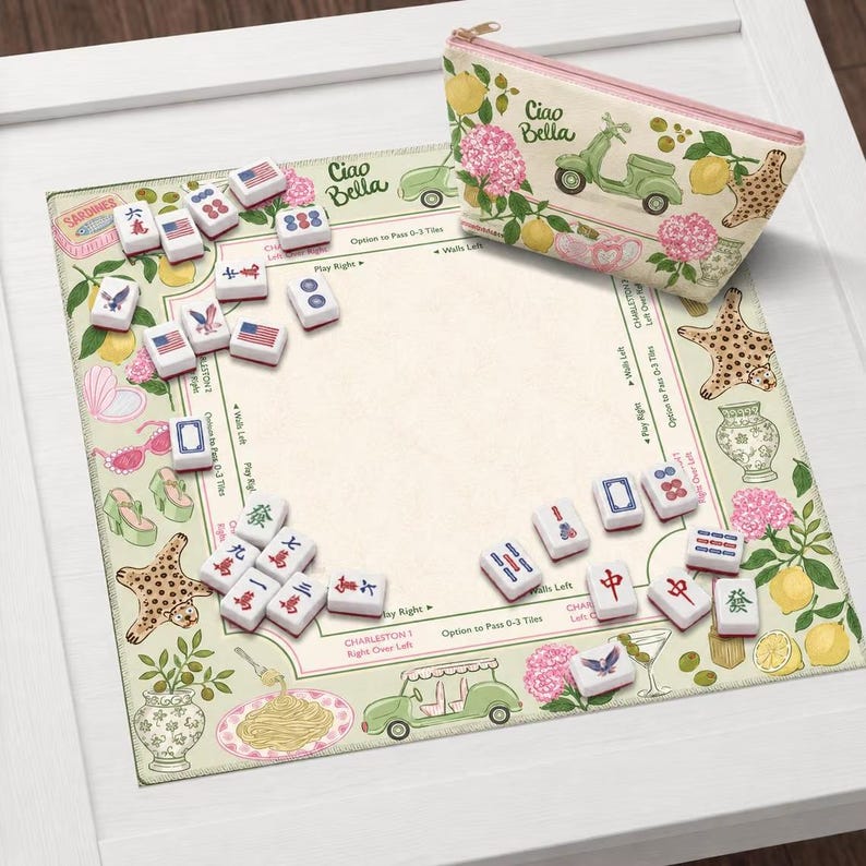 Puede incluir: Un juego de Mahjong con un tapete de color crema ilustrado con limones, hortensias rosas, un scooter verde y pasta. El set incluye fichas blancas con s&iacute;mbolos rojos, azules y negros, y un estuche con cremallera con la inscripci&oacute;n Ciao Bella.