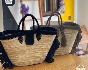 Puede incluir: Dos bolsos de mano de paja con detalles en negro y marrón. Los bolsos tienen cuerpos de paja tejida, asas de cuero y flecos. Uno tiene una solapa y flecos negros, el otro detalles marrones y una borla.