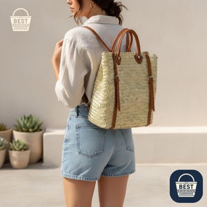 May include: A woven straw backpack with brown leather straps and handles. The bag has a rectangular shape and is worn on the back. The bag has a natural, light tan colour. The bag is handmade.