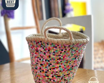May include: A small, handmade basket with a colorful sequined exterior. The basket features a woven design with a variety of colors, including pink, yellow, green, and blue. It has two woven handles and a natural-colored rim. The text "BEST HANDMADE" is visible.