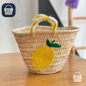 Może przedstawiać: Tkana torba typu tote ze słomy z żółto-białym paskiem. Torba posiada haftowaną żółtą cytrynę z zielonym liściem. Torba jest ręcznie robiona.
