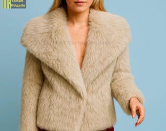 May include: A beige faux fur jacket with a wide collar. The jacket has a V-neck design and a soft, textured appearance. The Tartan Brigade logo is visible in the upper left corner.
