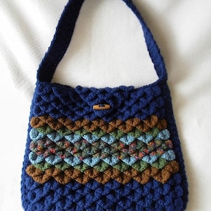 May include: A blue crocheted handbag with a brown, green, and blue patterned stripe. The bag has a single strap and a wooden button closure.