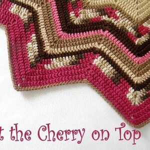 May include: A close-up of a crocheted star-shaped blanket with a pink, brown, and beige color scheme. The text "Pattern" is visible on the left side of the image and the text "Put the Cherry on Top" is visible at the bottom of the image.