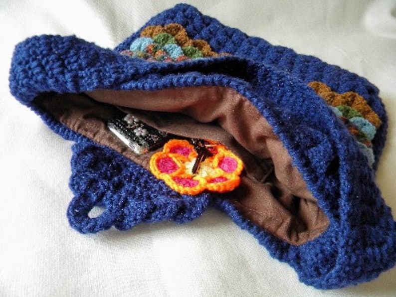 May include: A blue crocheted bag with a brown lining and a colorful crocheted flower design. The bag is open and shows a brown lining and a few items inside.