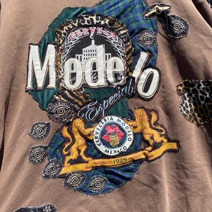 Op de afbeelding: Bruin sweatshirt met een grote, multi-textuur patch met de tekst "Modelo Especial" en een logo met leeuwen. Extra patches zijn voorzien van oog- en luipaardprint designs. De sweatshirt heeft een vintage uitstraling.