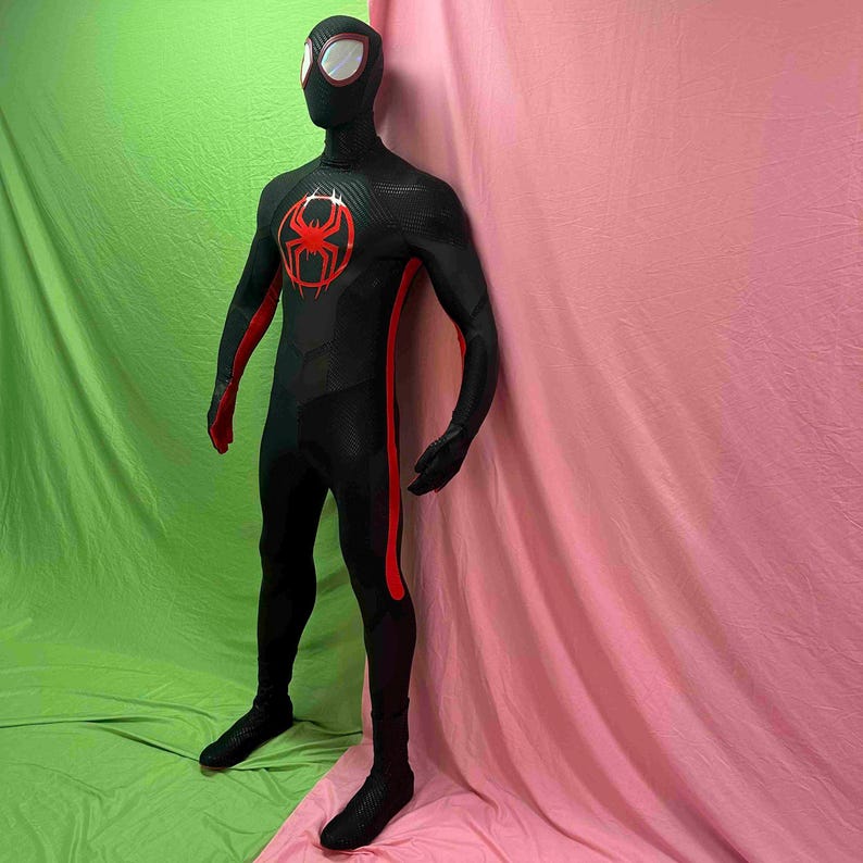 May include: A black superhero costume with red detailing, including a spider emblem on the chest. The costume has a full head covering with white eye details and red trim. The suit features red stripes down the sides and is made of a textured material.