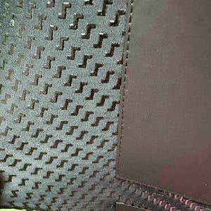 May include: Close-up of a textured fabric with a repeating pattern of dark grey shapes on a lighter grey background. A solid dark grey panel is on the right side, with a black seam separating the two sections.