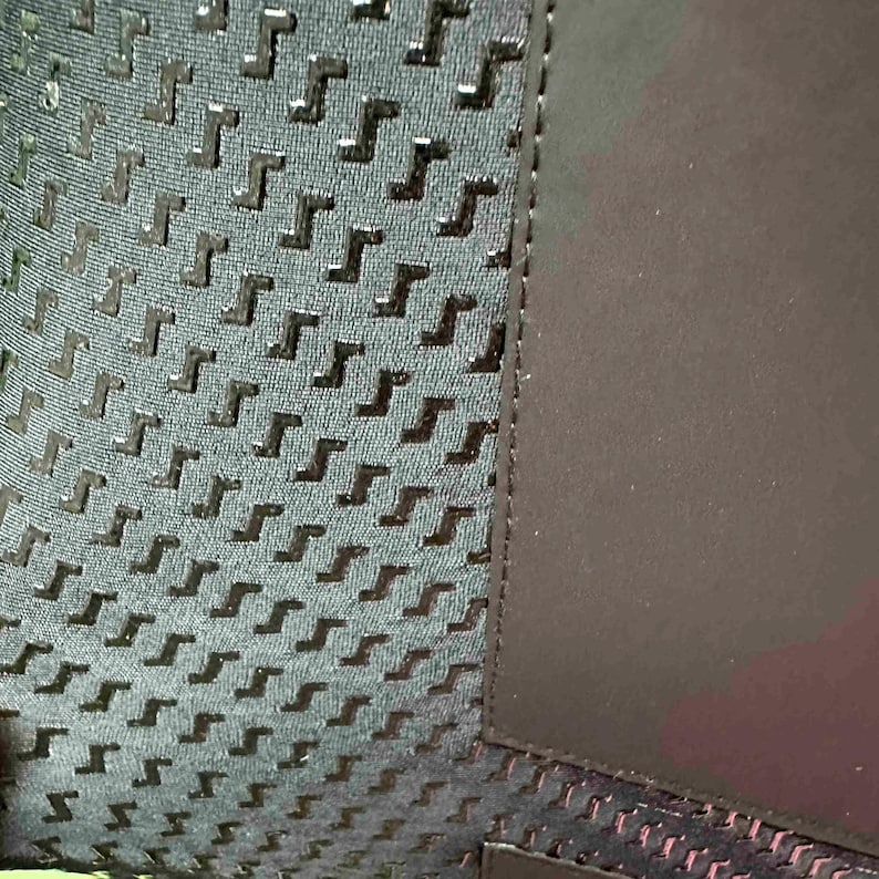 May include: Close-up of a textured fabric with a repeating pattern of dark grey shapes on a lighter grey background. A solid dark grey panel is on the right side, with a black seam separating the two sections.