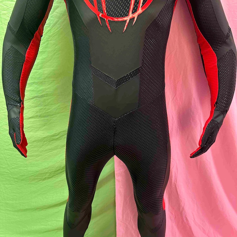 May include: A black and red bodysuit with a textured pattern. The suit has red accents on the arms and chest, with a detailed design on the upper back. The gloves are black with red detailing. The suit appears to be made of a flexible material.