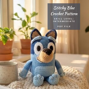 Pode incluir: Um brinquedo de crochê azul feito à mão com detalhes em castanho claro, sentado sobre um cobertor creme. A imagem inclui uma caneca, plantas e o texto "Stitchy Blue Crochet Pattern, Skill Level: Intermediate, PDF File."
