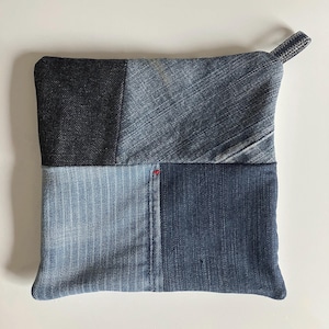 May include: A blue and black patchwork pot holder made from denim fabric. The pot holder has a loop handle for easy hanging.
