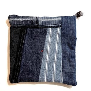May include: A blue denim patchwork zippered pouch with a gray zipper pull. The pouch is made from different shades of blue denim and has a striped pattern on one side.