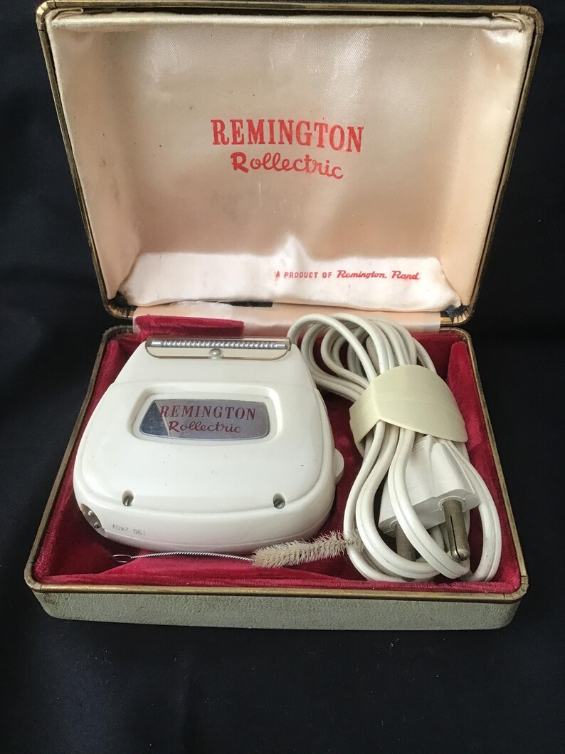 May include: A vintage Remington Rollectric electric shaver in its original case. The white shaver has a silver blade and is housed in a red velvet-lined case with the Remington Rollectric logo in red. A cleaning brush and power cord are included.