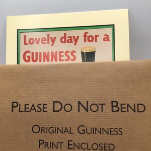 Puede incluir: Una impresi&oacute;n enmarcada con el texto "Lovely day for a GUINNESS" y una imagen de una pinta de Guinness. La impresi&oacute;n est&aacute; en un marco color crema, y el embalaje dice "PLEASE Do Not BEND" y "ORIGINAL GUINNESS PRINT ENCLOSED."