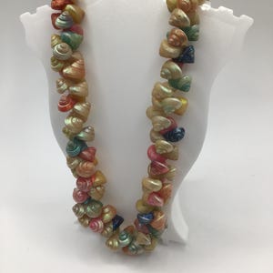 May include: A necklace composed of spiral-shaped shells in various colours, including orange, pink, yellow, green, and blue. The necklace is displayed on a white jewellery bust.