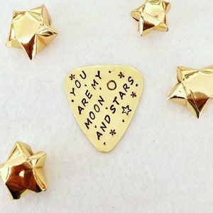 May include: Gold-coloured metal stars and a guitar pick with the text "You are my moon and stars."