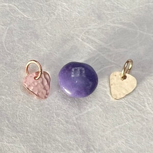May include: Three small charms, one is a purple candy-like charm, one is a gold-coloured charm shaped like a guitar pick, and one is a pink charm shaped like a heart.