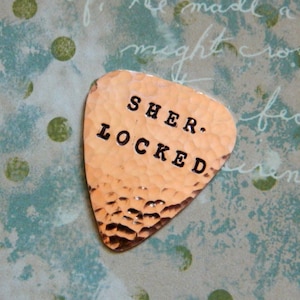 May include: A copper guitar pick with the words "Sher. Locked" stamped on it.