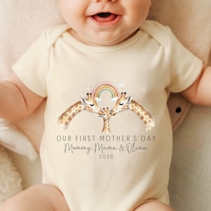 May include: Cream-colored baby bodysuit with a giraffe family design and a rainbow. The text reads "OUR FIRST MOTHER'S DAY" and "Mommy, Mama & Olivia 2026". The bodysuit is short-sleeved and has a snap closure.