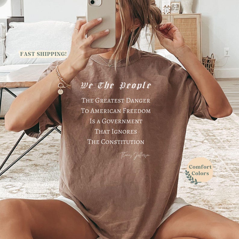 Puede incluir: Camiseta marr&oacute;n con el texto "We The People" y una cita de Thomas Jefferson. La cita dice: "El mayor peligro para la libertad estadounidense es un gobierno que ignora la Constituci&oacute;n."