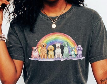 Puede incluir: Una camiseta de manga corta gris carbón con un gráfico de acuarela colorido de siete razas de perros diferentes de pie en fila bajo un arcoíris vibrante. Los perros incluyen un bulldog, un golden retriever, un caniche y otras razas.