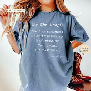 Puede incluir: Una camiseta azul polvorienta con la cita "We The People" y una cita de Thomas Jefferson. El texto dice: "El mayor peligro para la libertad estadounidense es un gobierno que ignora la Constituci&oacute;n."