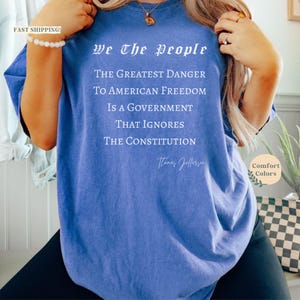 Puede incluir: Una camiseta azul con el texto "We The People" y una cita de Thomas Jefferson. La cita dice: "El mayor peligro para la libertad estadounidense es un gobierno que ignora la Constituci&oacute;n."