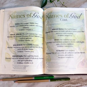May include: An open book with pages titled Names of God and Names of God Cont. featuring printed text defining names like Elohim, Yahweh, Jehovah Jireh, Jehovah Rapha, Jehovah Shalom, El Roi, and El Shaddai, with two colored pencils placed below.